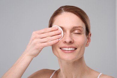 Beautiful woman removing makeup with cotton pad on gray background