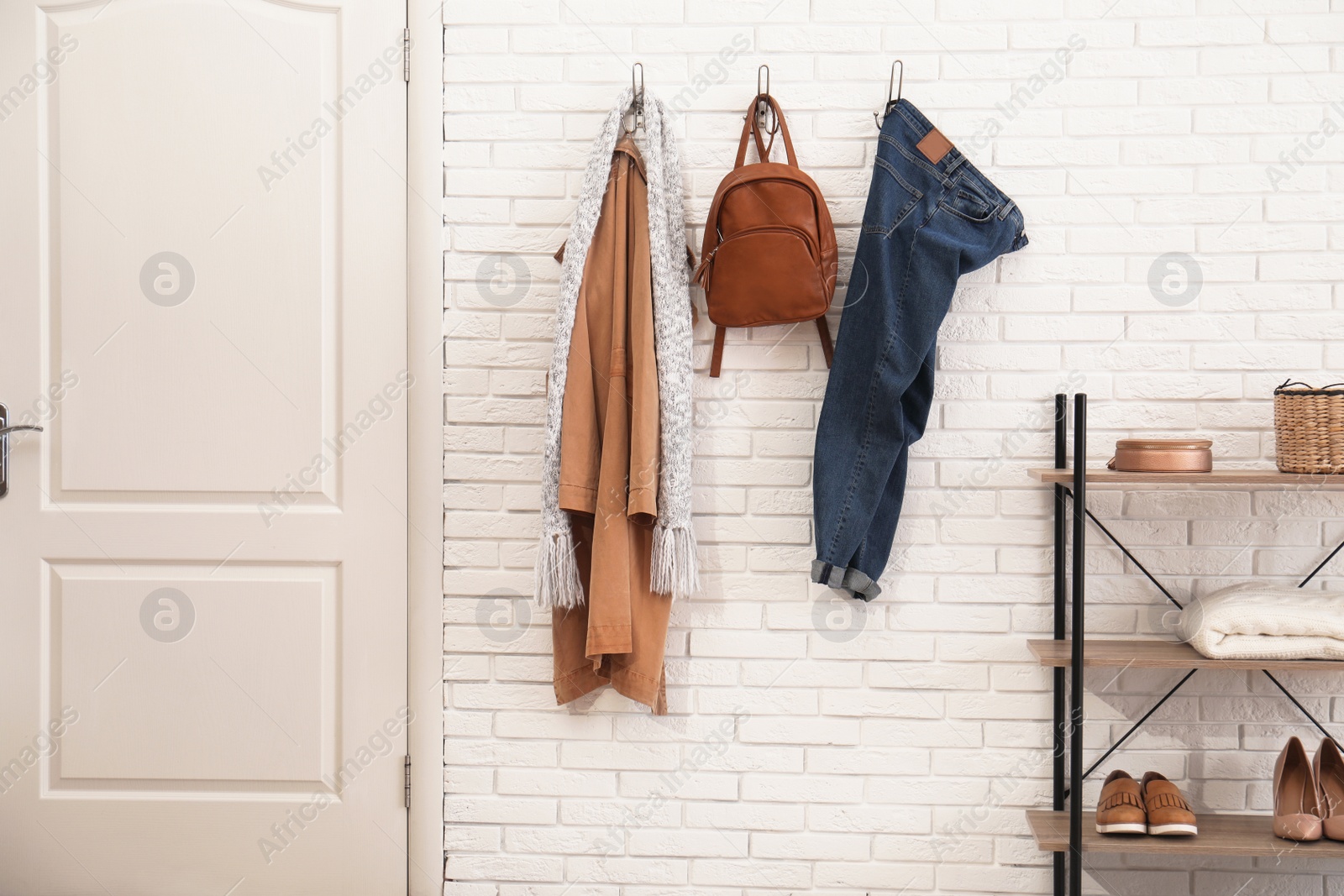 Photo of Stylish hallway interior with door, comfortable furniture and clothes on brick wall