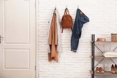 Photo of Stylish hallway interior with door, comfortable furniture and clothes on brick wall