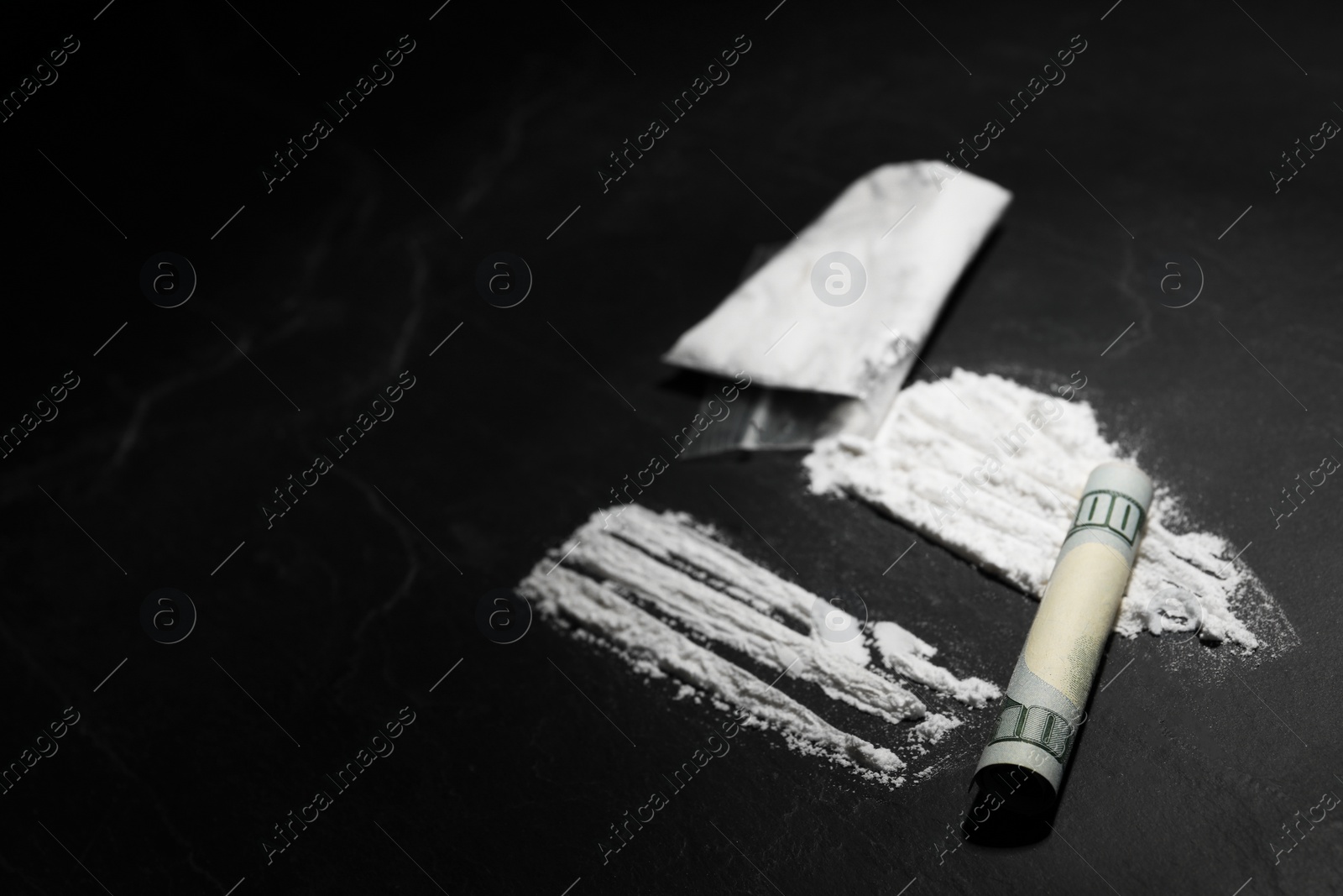 Photo of Plastic bag with hard drug and rolled dollar banknote on dark table, closeup. Space for text
