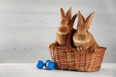 Photo of Cute bunnies, basket and Easter eggs on white table. Space for text