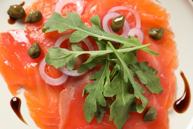 Photo of Delicious salmon carpaccio with arugula, capers and onion on white background, top view