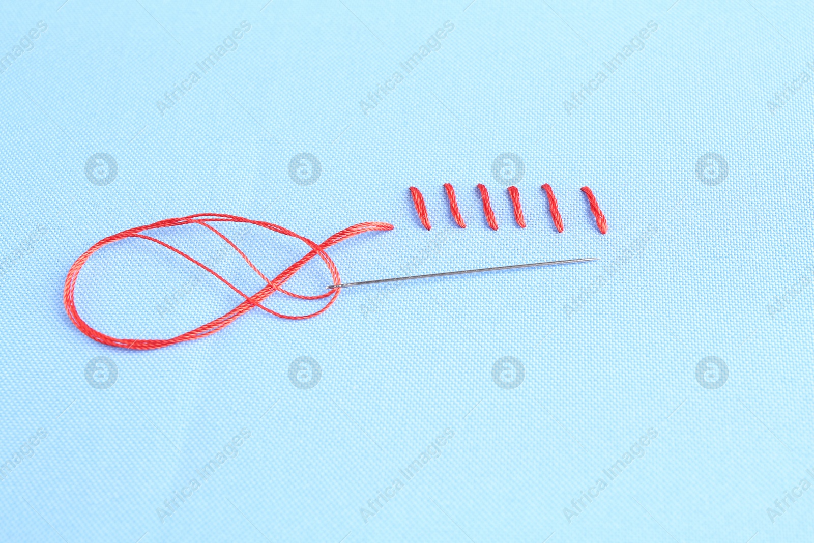 Photo of Sewing needle with thread and stitches on light blue cloth, above view