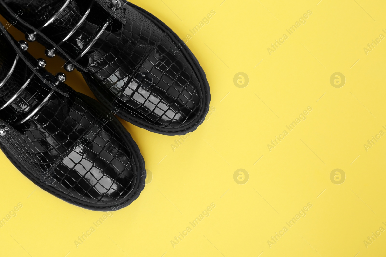 Photo of Pair of stylish ankle boots on yellow background, top view. Space for text