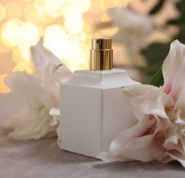 Bottle of perfume and beautiful lily flowers on table against beige background with blurred lights, closeup