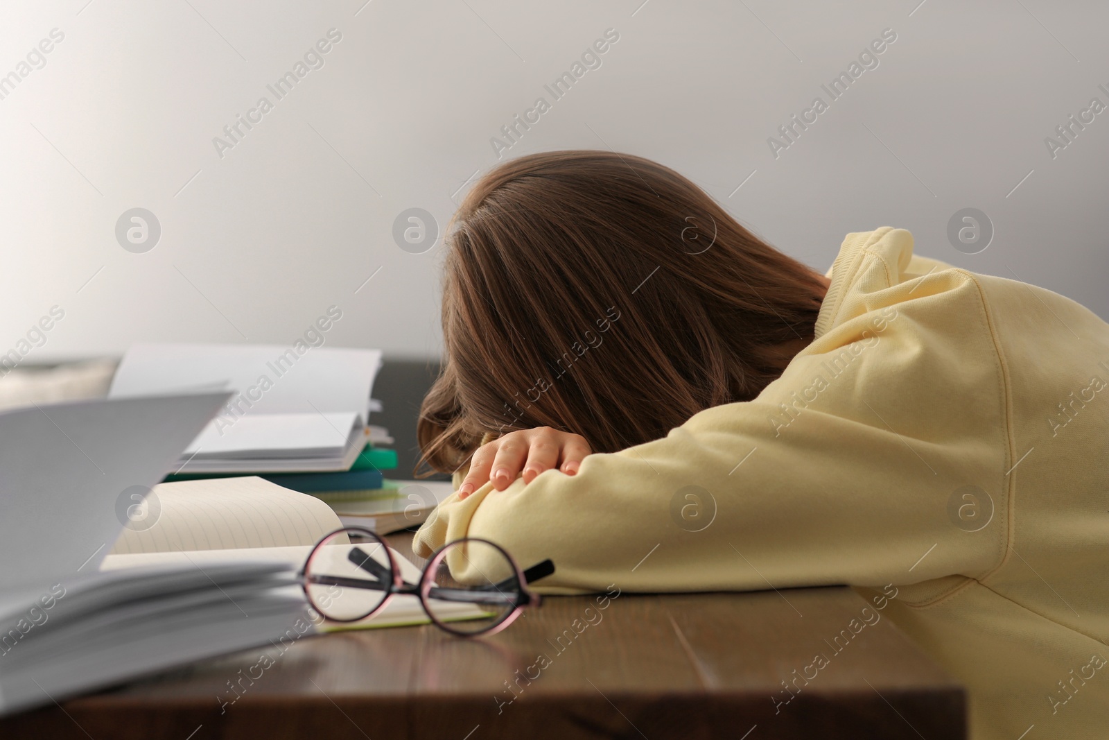 Photo of Young tired woman sleeping near books at wooden table indoors