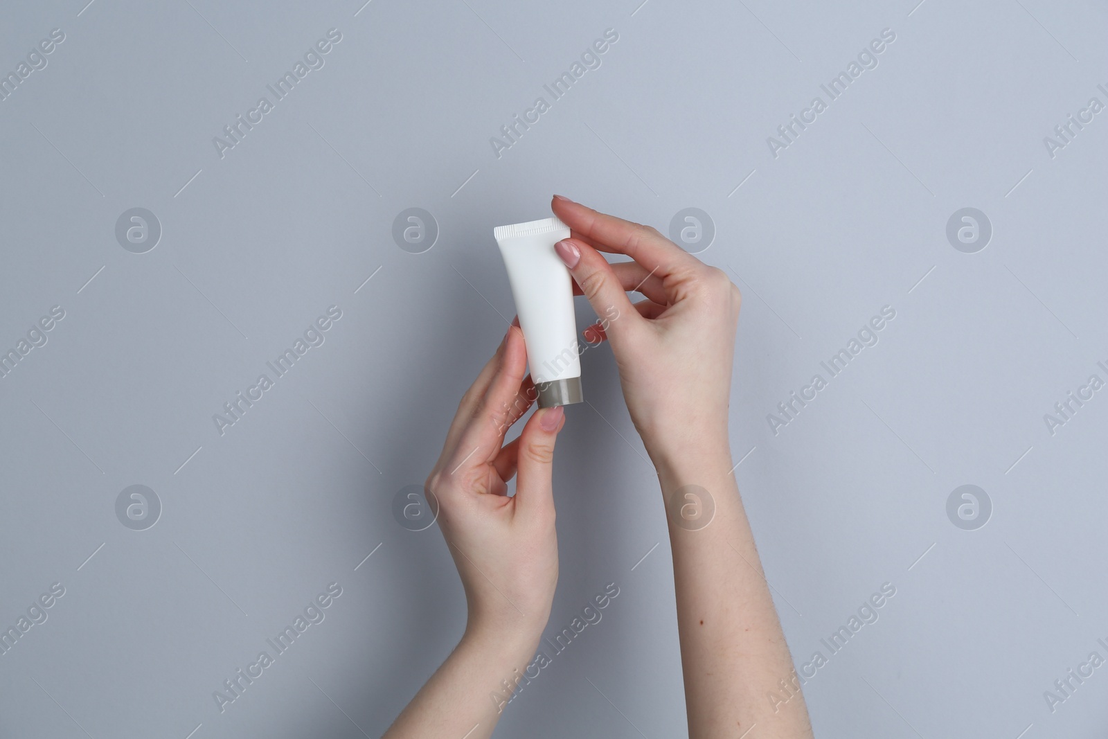 Photo of Woman holding tube of cream on grey background, closeup