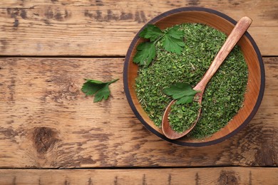 Photo of Bowl and spoon with dried parsley on wooden table, top view. Space for text