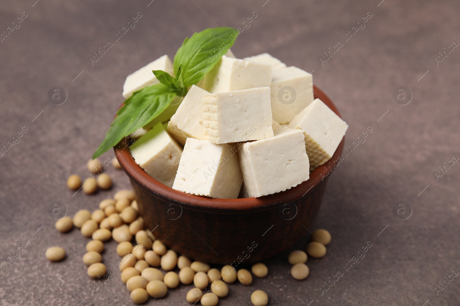 Photo of Delicious tofu cheese, basil and soybeans on brown textured table, closeup