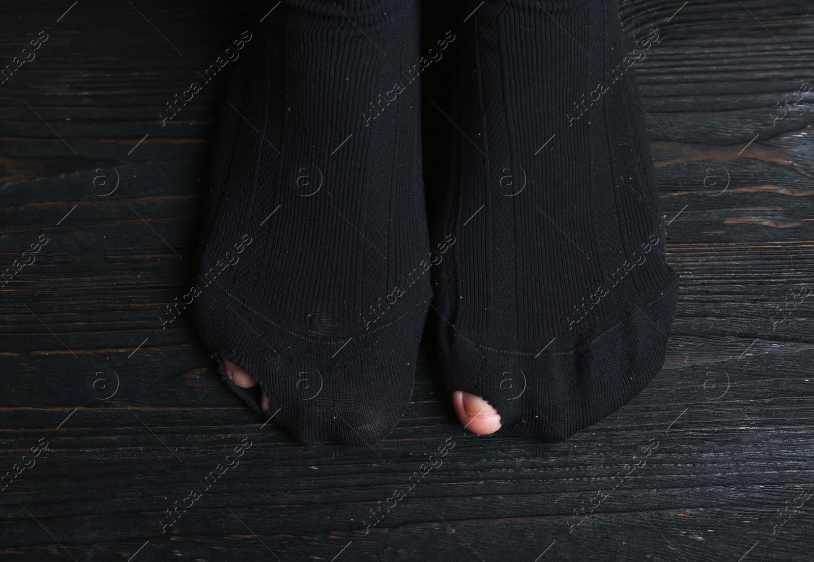 Photo of Poor person in shabby socks on wooden floor, closeup