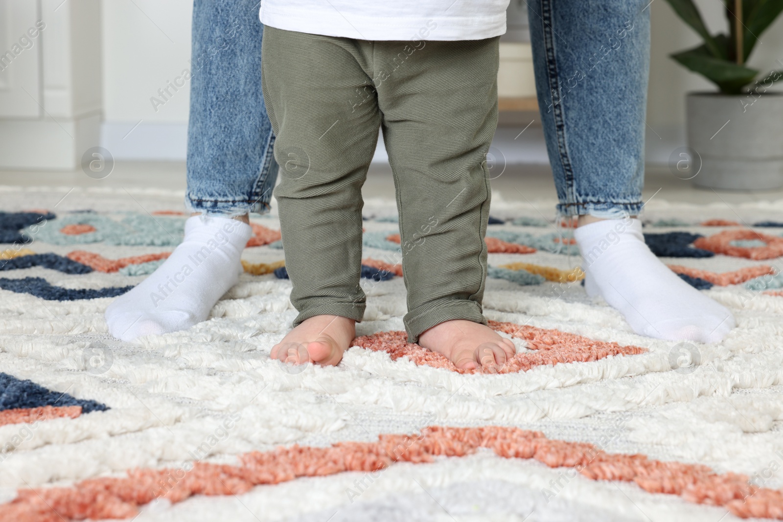 Photo of Mother supporting her son while he learning to walk on carpet indoors, closeup