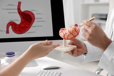 Gastroenterologist with human stomach model consulting patient at table in clinic, closeup