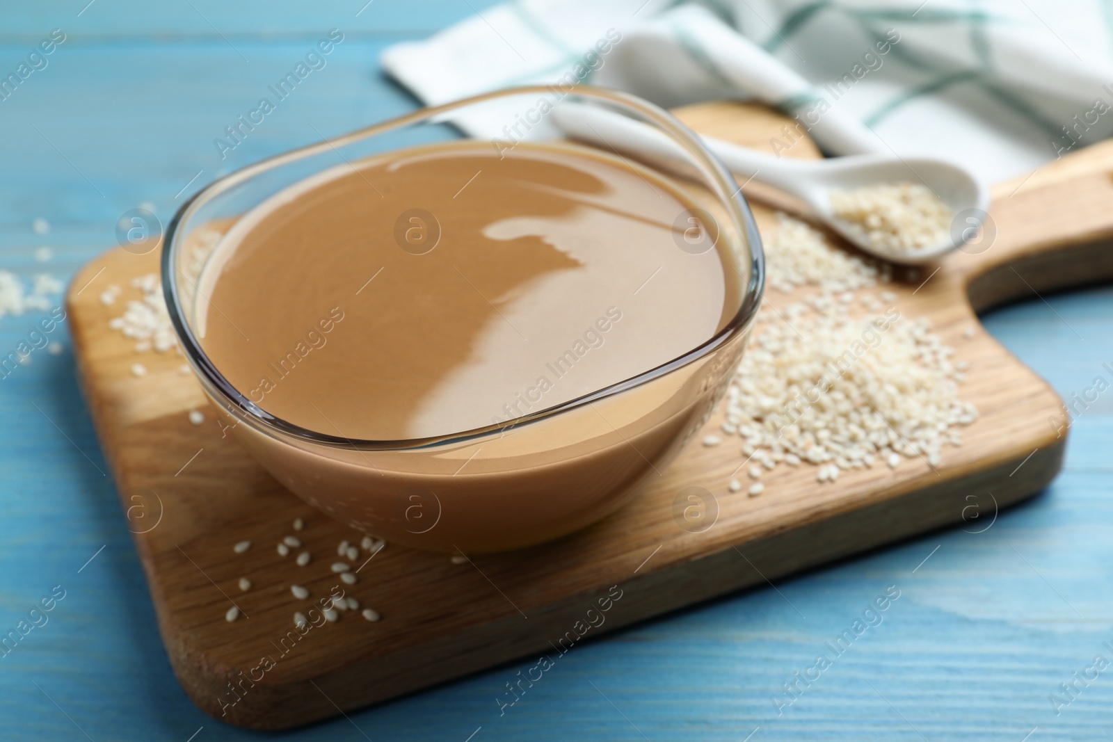 Photo of Tasty sesame paste and seeds on light blue wooden table