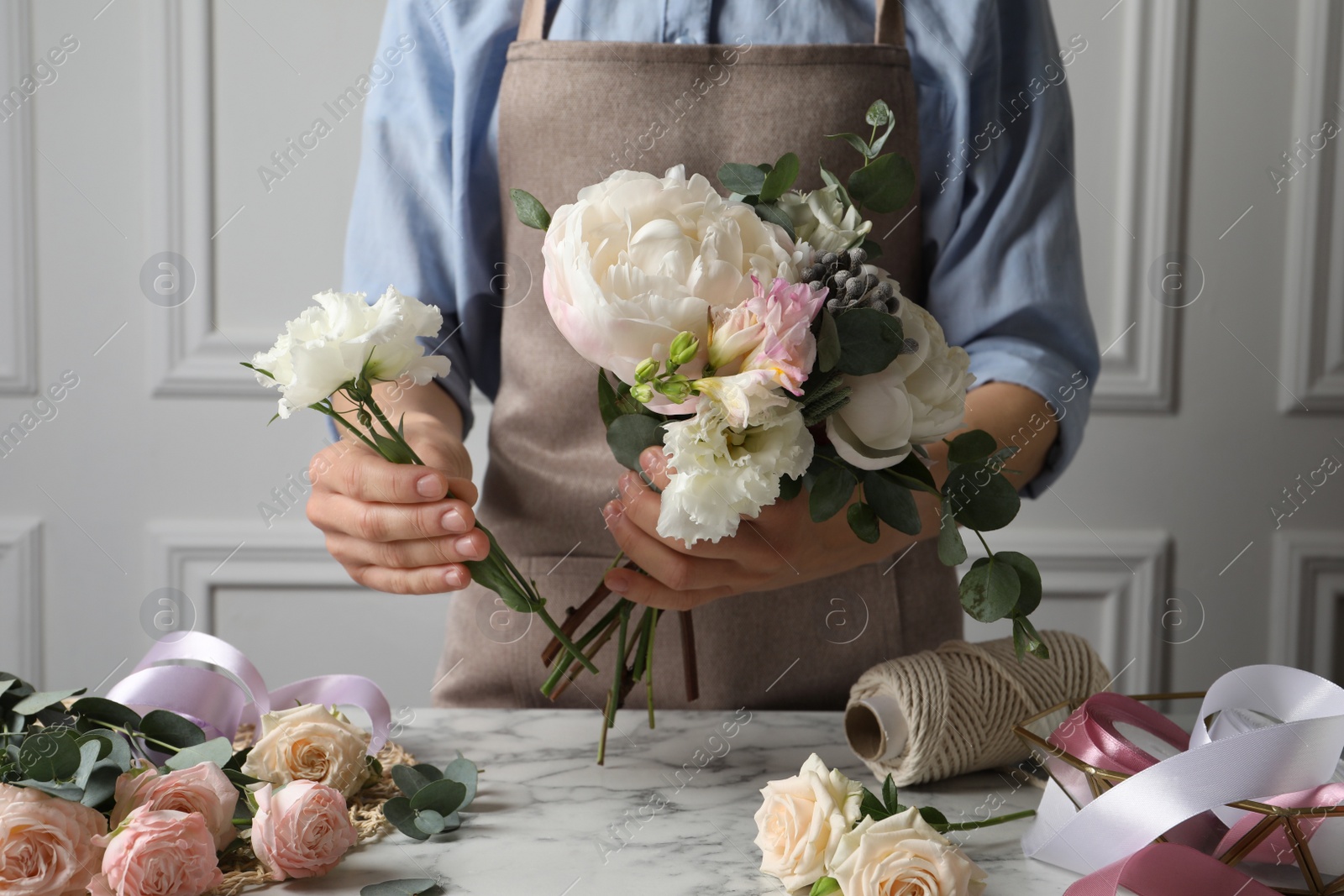Photo of Florist creating beautiful bouquet at white marble table, closeup