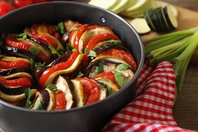 Photo of Delicious ratatouille in round baking pan on table, closeup