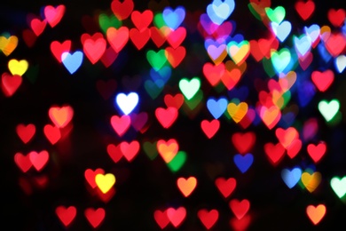 Blurred view of colorful heart shaped lights on black background