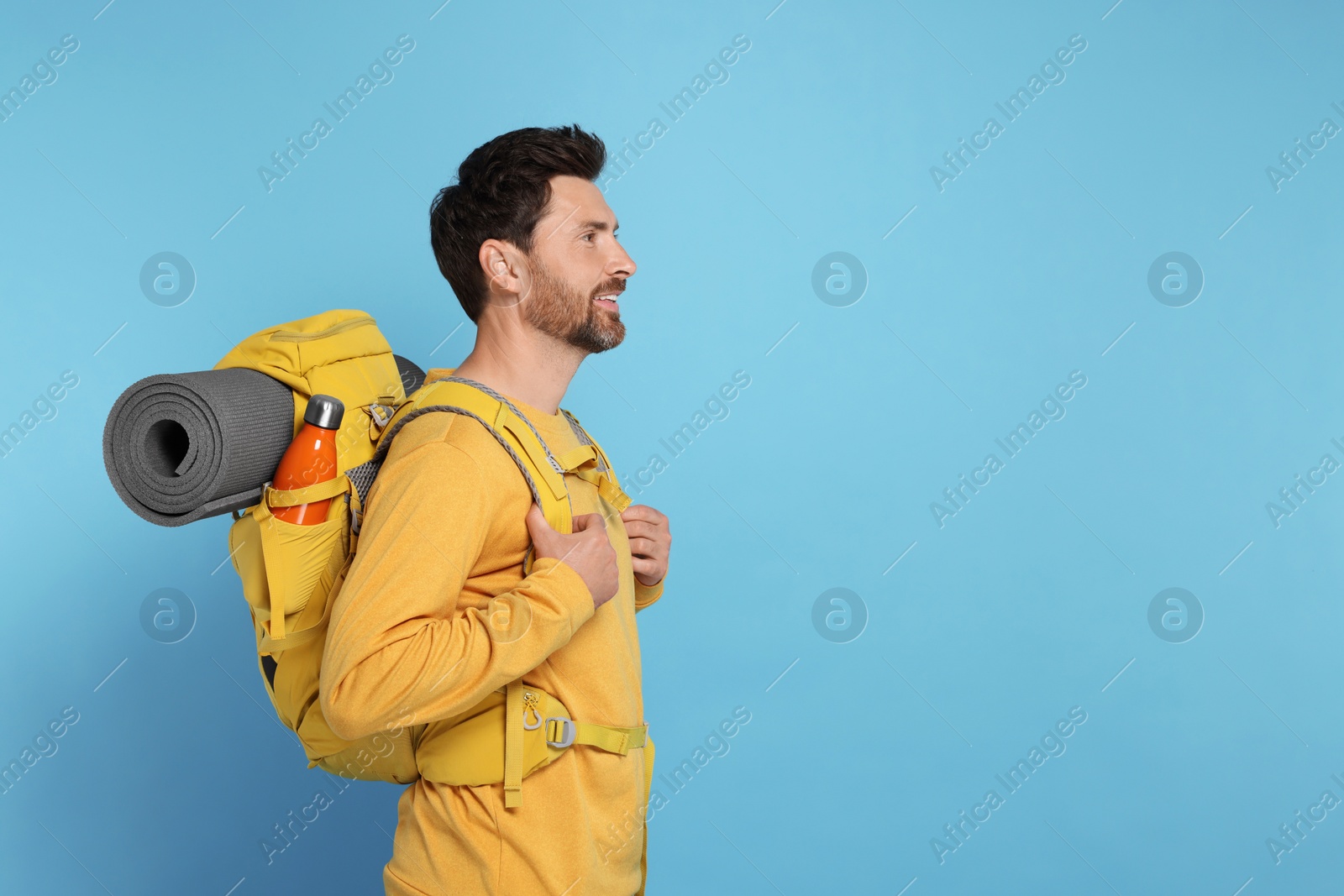 Photo of Happy man with backpack on light blue background, space for text. Active tourism