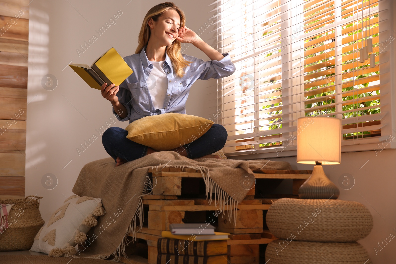 Photo of Beautiful young woman reading book near window at home