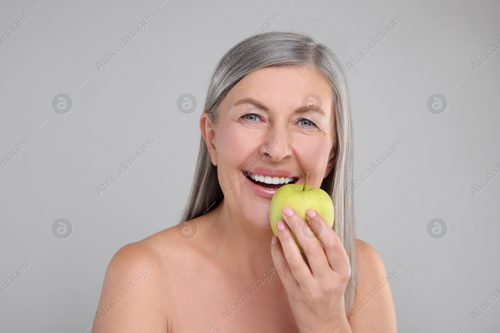 Photo of Beautiful woman with fresh apple on grey background. Vitamin rich food