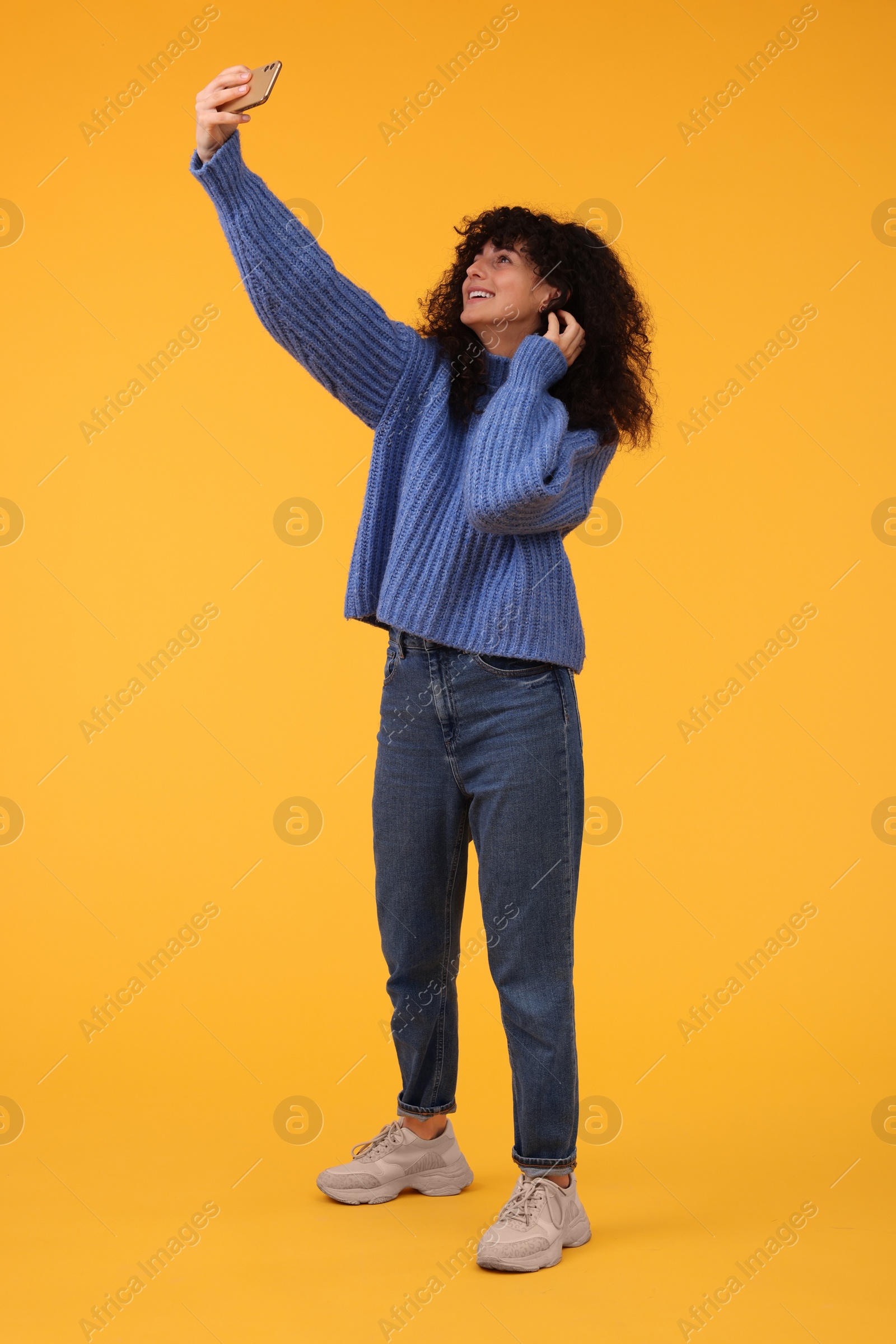 Photo of Beautiful young woman taking selfie with smartphone on orange background