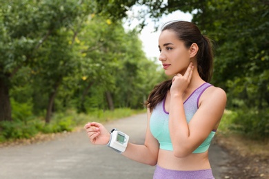 Young woman checking pulse with medical device after training in park. Space for text