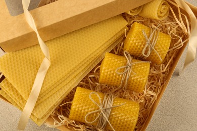 Photo of Beautiful yellow beeswax candles and sheets in box on light textured table, top view