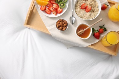 Photo of Tasty breakfast served in bed. Oatmeal, juice, fruits, almonds and honey on tray, top view. Space for text