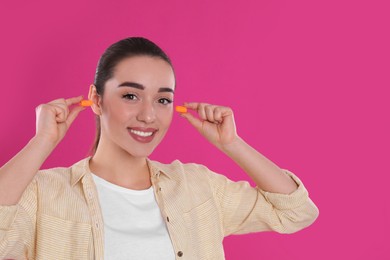 Photo of Young woman inserting foam ear plugs on pink background