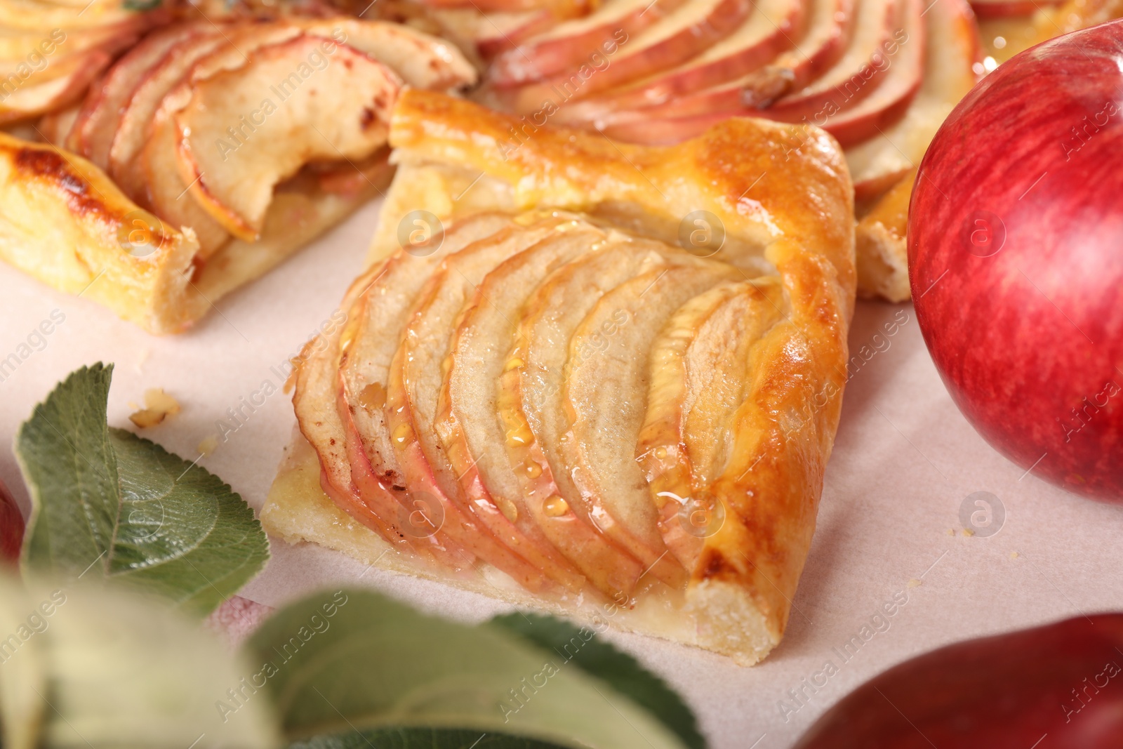 Photo of Piece of tasty apple pie, fresh fruits and green leaves on table, closeup