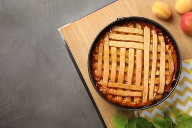 Delicious apricot pie in baking dish and fresh fruits on grey table, flat lay. Space for text