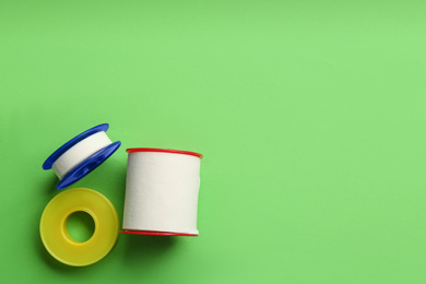 Photo of Sticking plaster rolls on green background, flat lay. Space for text