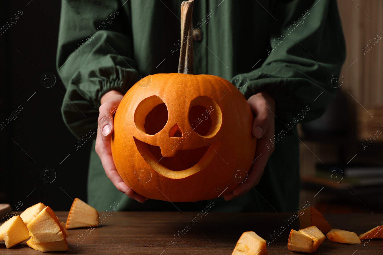 Photo of Woman holding carved pumpkin for Halloween at wooden table indoors, closeup