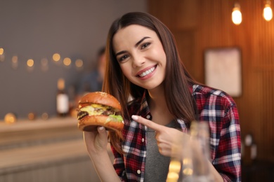 Young woman eating tasty burger in cafe