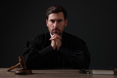 Judge with gavel and book sitting at wooden table against black background