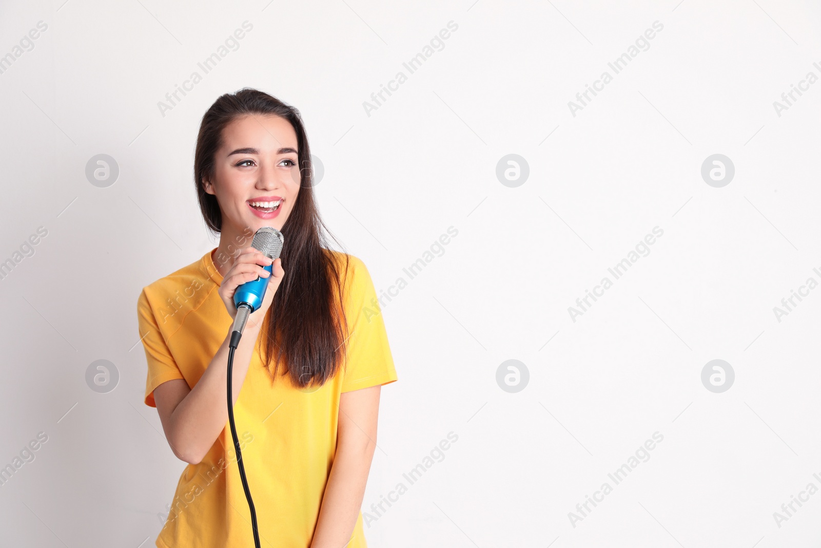 Photo of Young woman in casual clothes posing with microphone on color background. Space for text