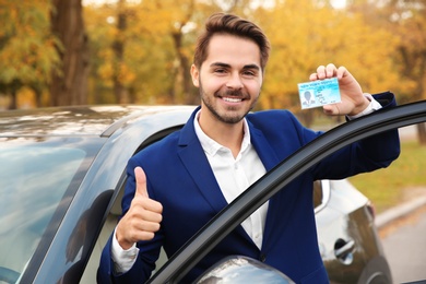 Photo of Young man holding driving license near open car