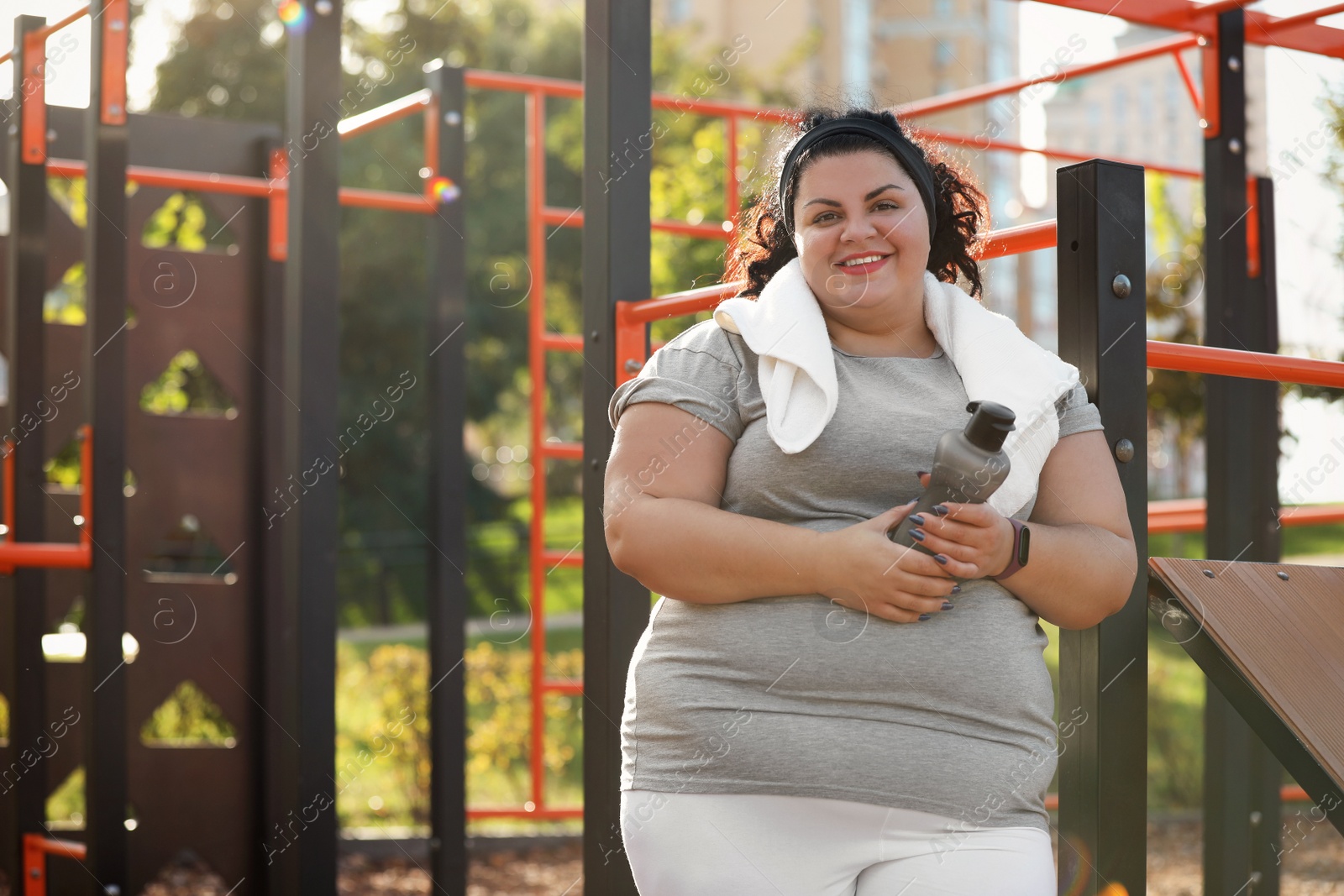 Photo of Beautiful overweight woman with towel and bottle on sports ground