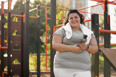 Beautiful overweight woman with towel and bottle on sports ground