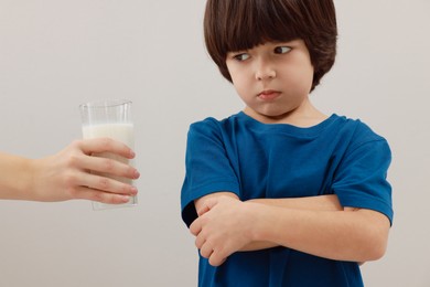 Photo of Cute little boy refusing to drink milk on grey background