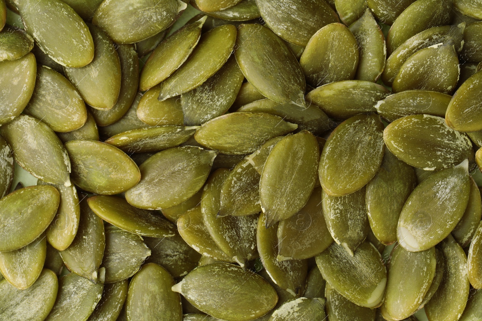 Photo of Many peeled pumpkin seeds as background, top view