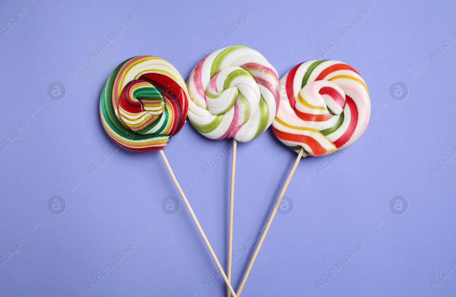 Photo of Sticks with different colorful lollipops on violet background, flat lay