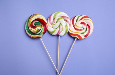 Sticks with different colorful lollipops on violet background, flat lay