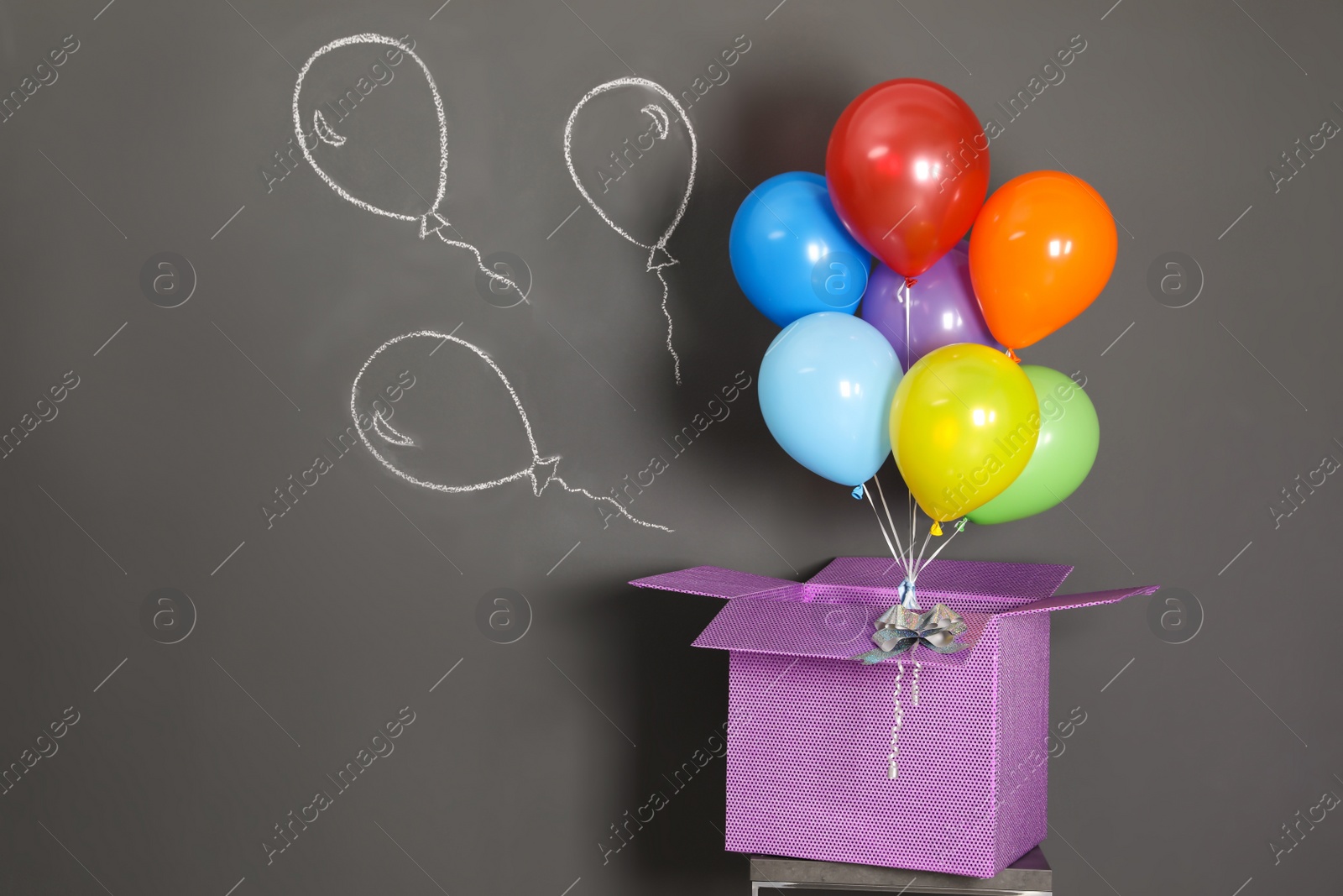 Photo of Gift box with bright air balloons and chalk drawing on grey background