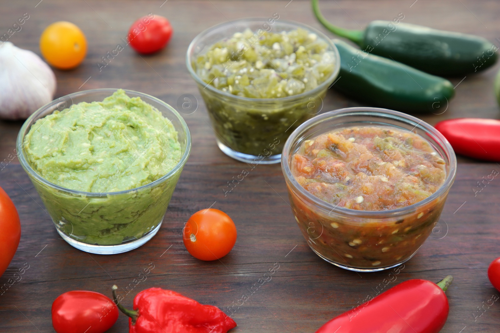 Photo of Tasty salsa sauces and ingredients on wooden table, closeup