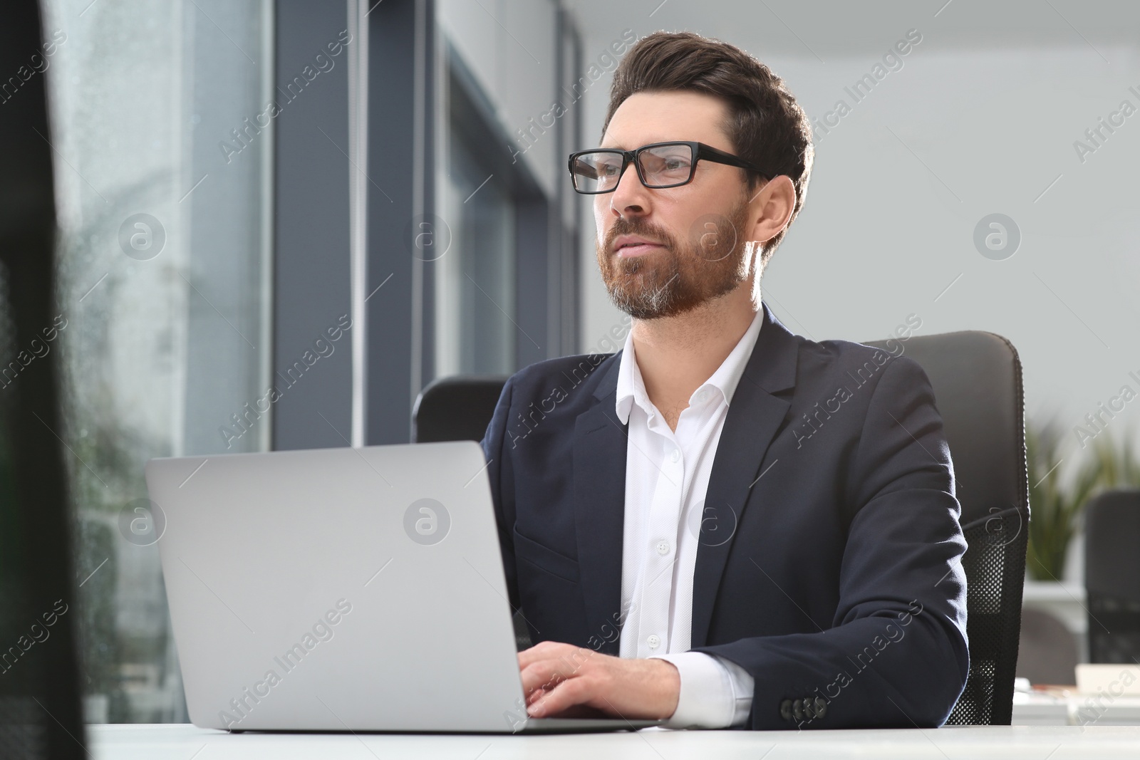 Photo of Man working on laptop at white desk in office