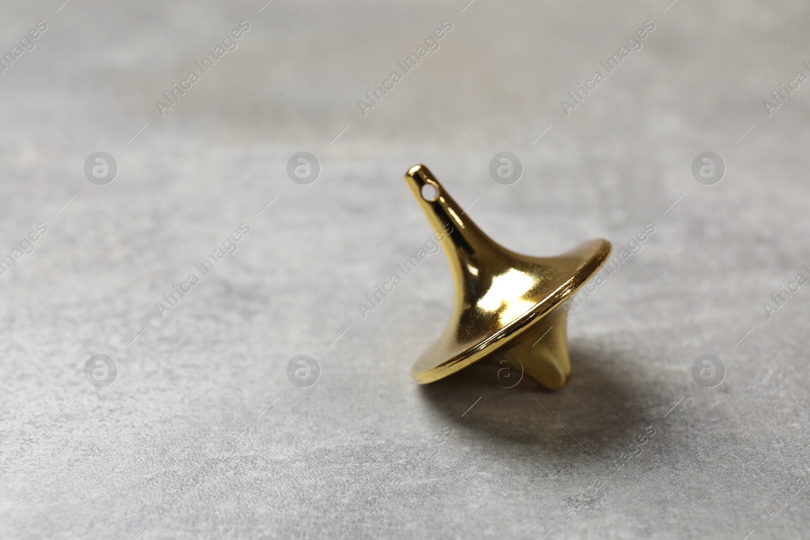Photo of One golden spinning top on grey textured background, closeup. Space for text