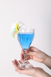 Woman holding glass of cocktail decorated with cotton candy and sour rainbow belt on white background, closeup