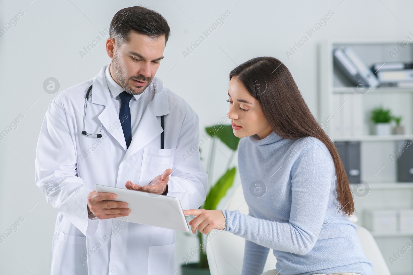 Photo of Doctor with tablet consulting patient in clinic