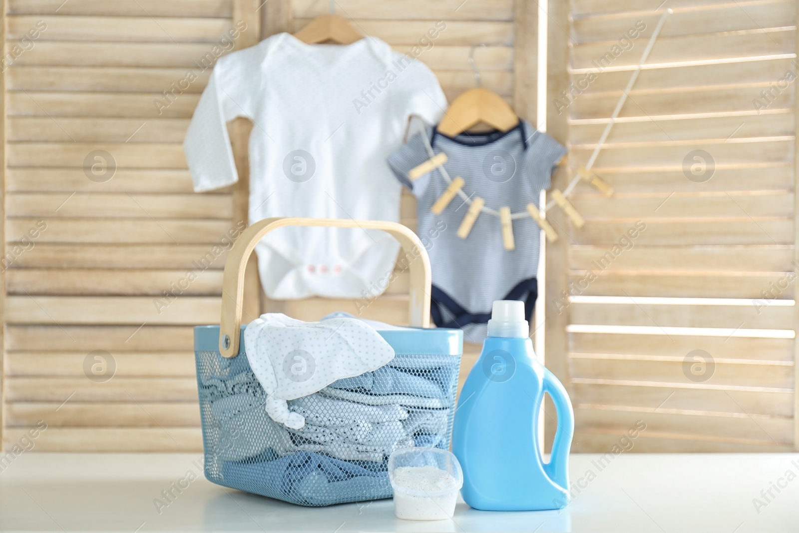 Photo of Basket with baby laundry, bottle of detergent and washing powder on white table