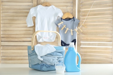 Basket with baby laundry, bottle of detergent and washing powder on white table